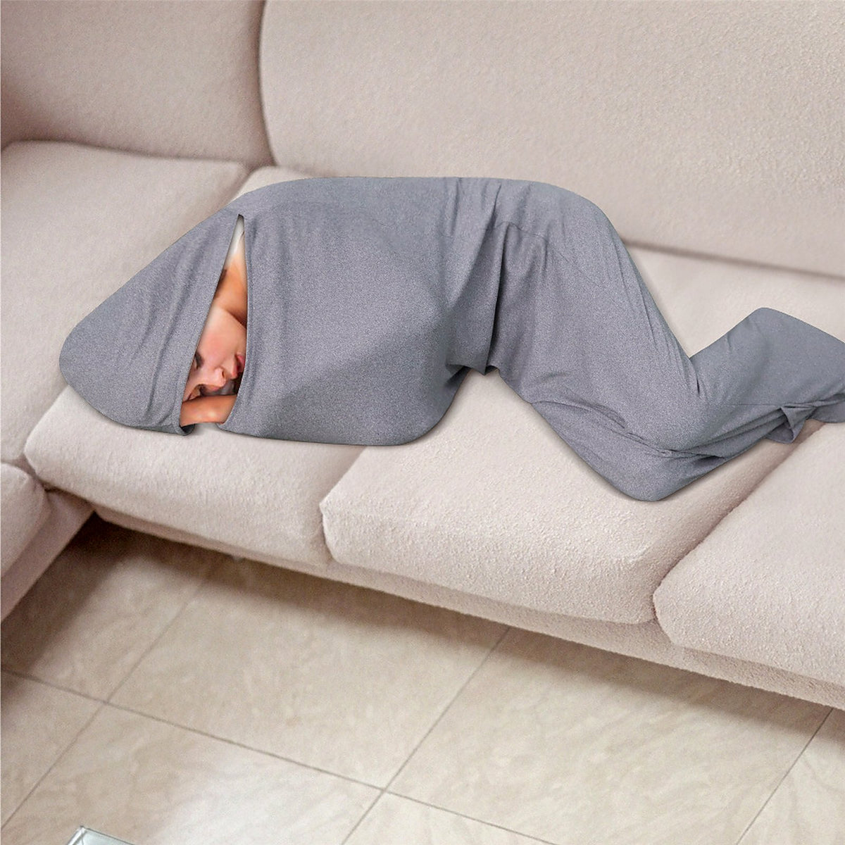 Adult resting on the sofa fully wrapped in the NESTLY sleep sack with the hood up